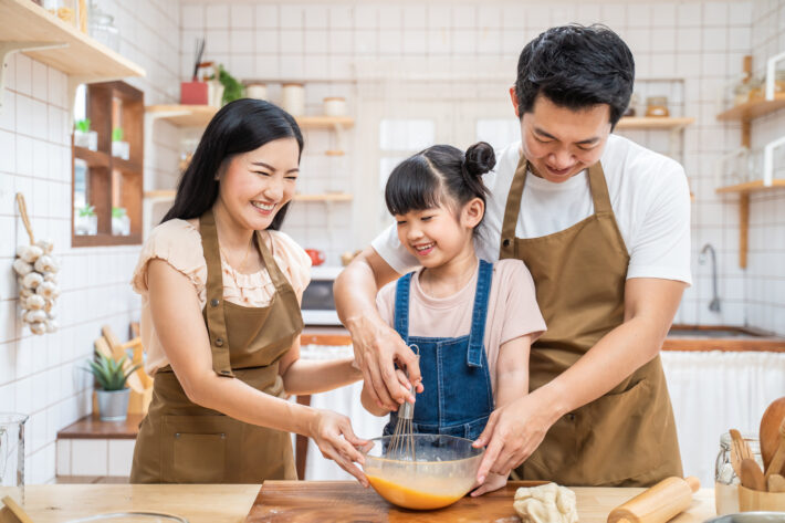 Asian happy family stay at home in kitchen, baking bakery and foods. Young little girl kid daughter learn to cook foods from parents, father and mother enjoy parenting activity relationship in house.