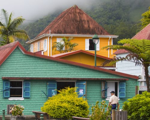 Colorful houses nestled in a lush mountain village with a person enjoying a leisurely walk.